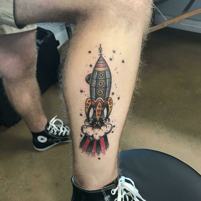 American traditional tattoo of a colorful rocket ship blasting off on a leg.