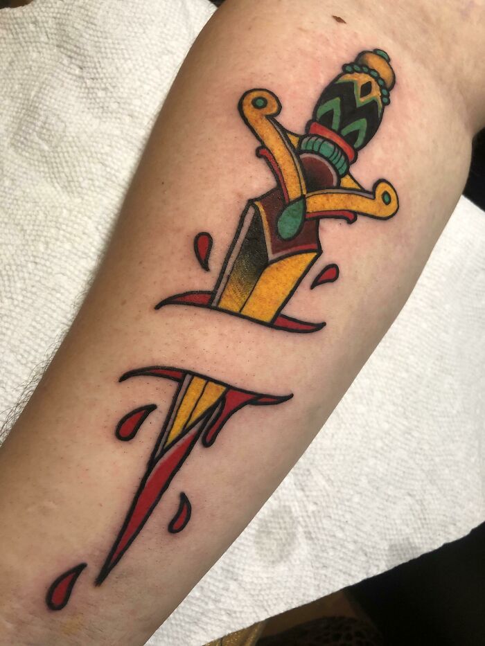 Colorful American traditional tattoo of a dagger with blood drops on skin, showcasing bold design elements.