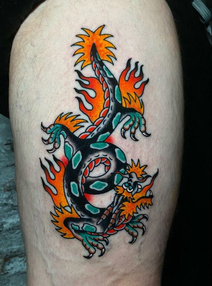 American traditional tattoo featuring a colorful dragon design with flames and bold outlines on the skin.