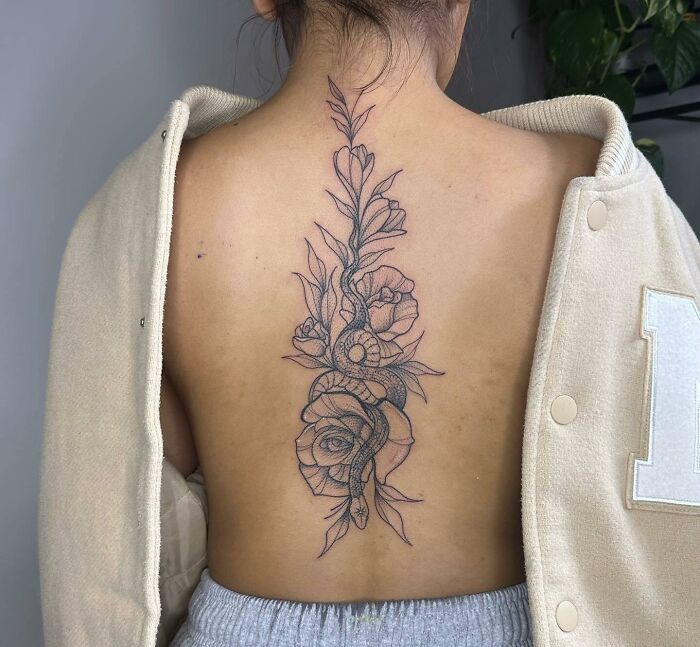 Ornate spine tattoo with floral and snake design on woman's back, showcasing intricate detail.