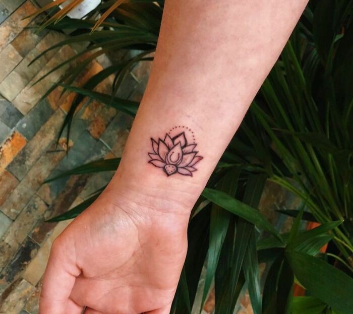 Lotus flower wrist tattoo among green plants, showcasing timeless accessory ideas.