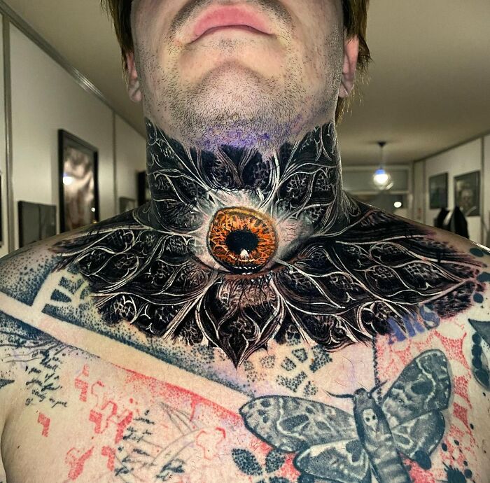 Neck tattoo art featuring a detailed eye design with surrounding ornate patterns in an indoor setting.