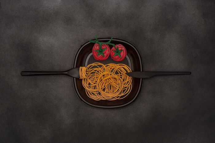 Plate with pasta and tomatoes symbolizing global problems creatively arranged with cutlery on dark background