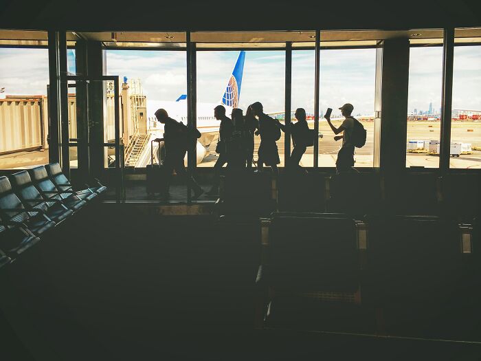 Silhouettes of travelers walking in an airport terminal near a plane, related to flight attendants and passenger experiences.