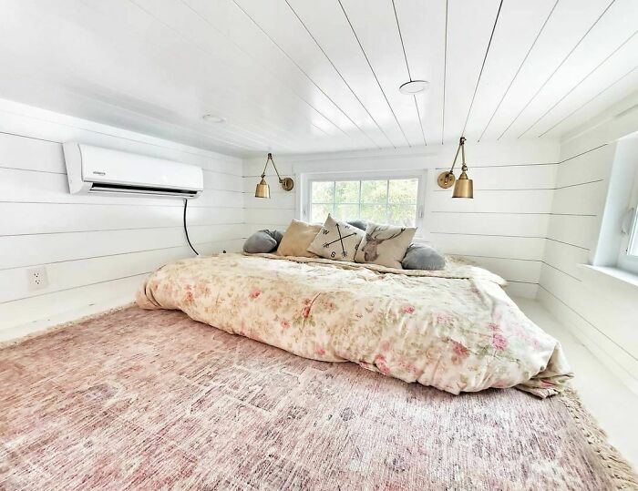 Cozy white tiny house bedroom with floral bedding, decorative pillows, and soft natural light from windows.