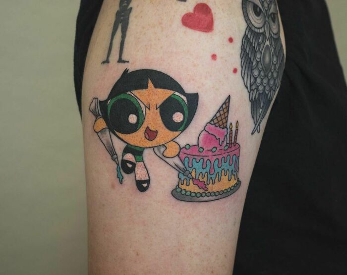 Buttercup character decorating a colorful cake in a watercolor tattoo, featuring vibrant food ink-spiration design.