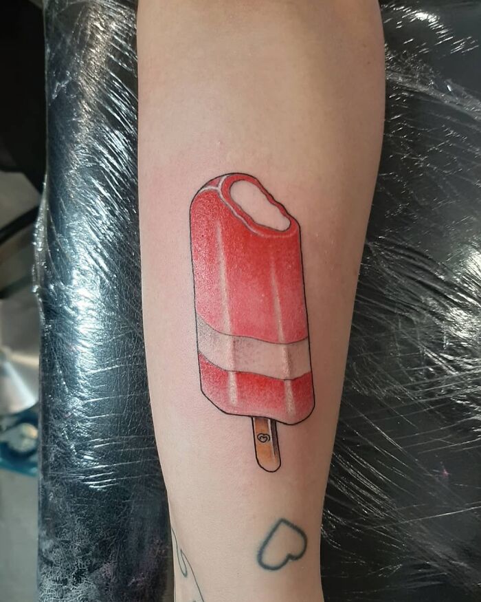 Food tattoo of a red popsicle with a bite on a forearm, capturing delicious ink art.
