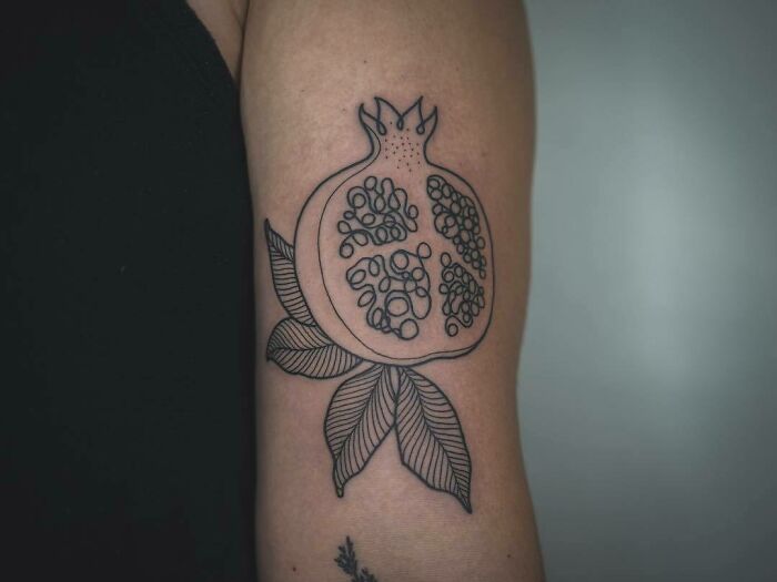 Pomegranate food tattoo with detailed seeds and leaves design on the arm.