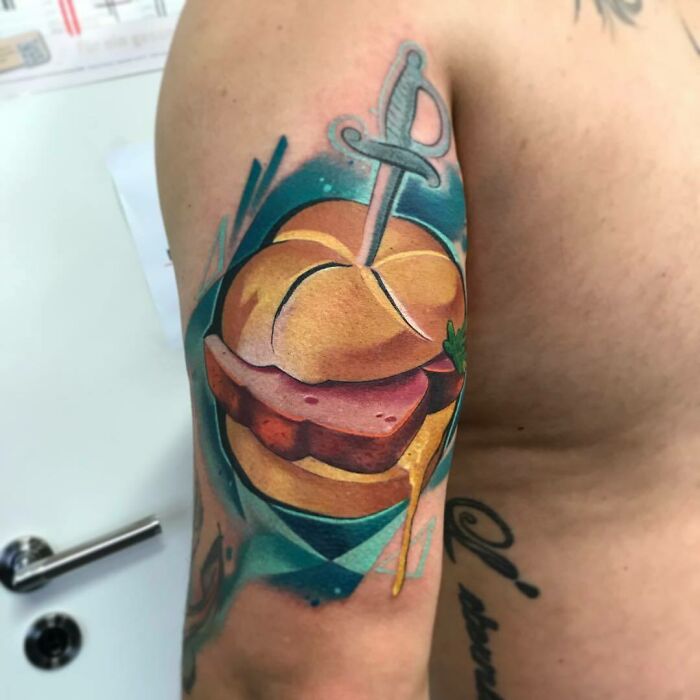 Food tattoo of a colorful sandwich with a sword, inked vividly on an arm, showcasing delicious food art.