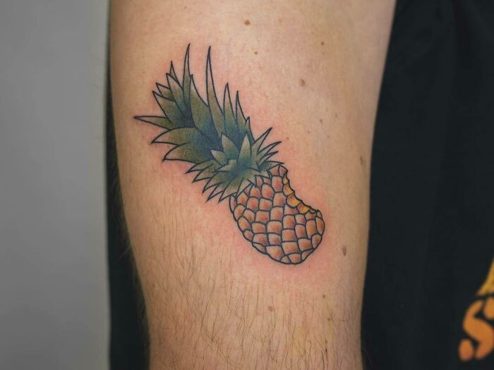 Pineapple food tattoo on upper arm, showcasing vibrant green and yellow colors.