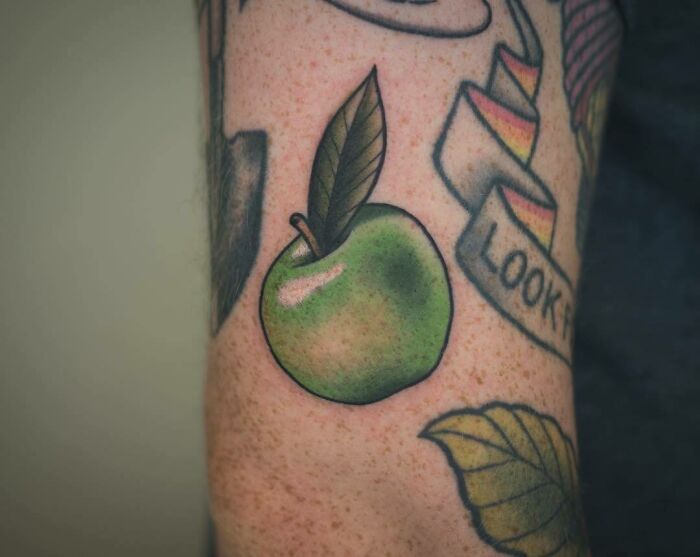 Green apple food tattoo with vibrant colors and realistic detail, located on a person's arm.