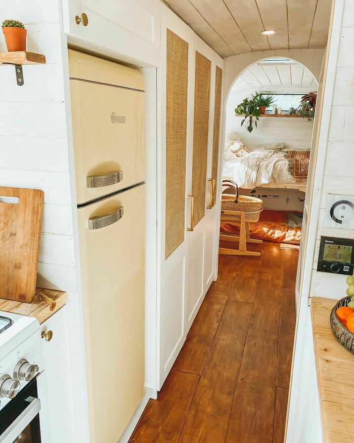 Beige fridge next to white cabinets in a cozy tiny house design with wooden flooring and a view of the bedroom area.