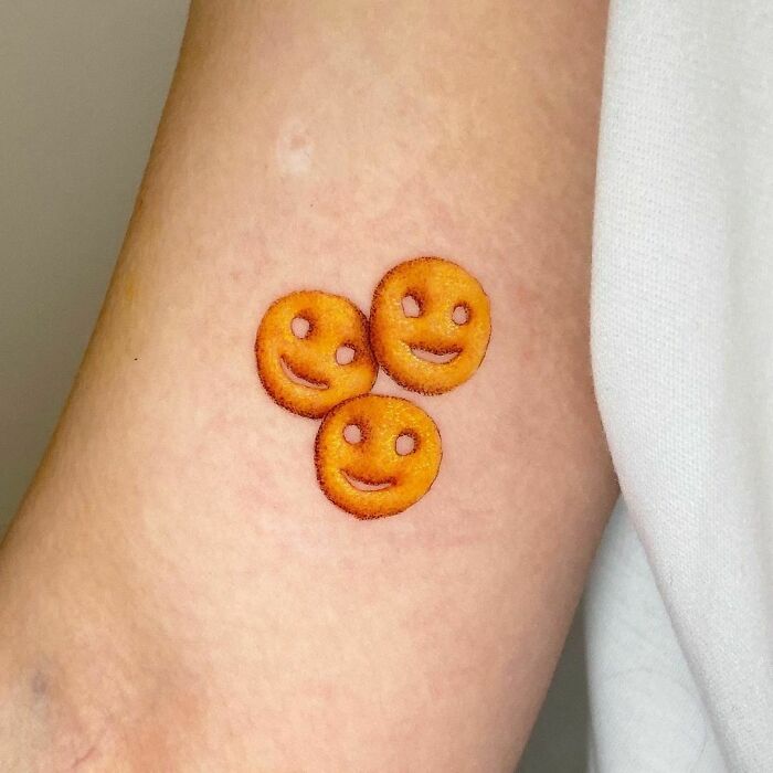 Tattoo of three smiley face fries on skin, inspired by delicious food.