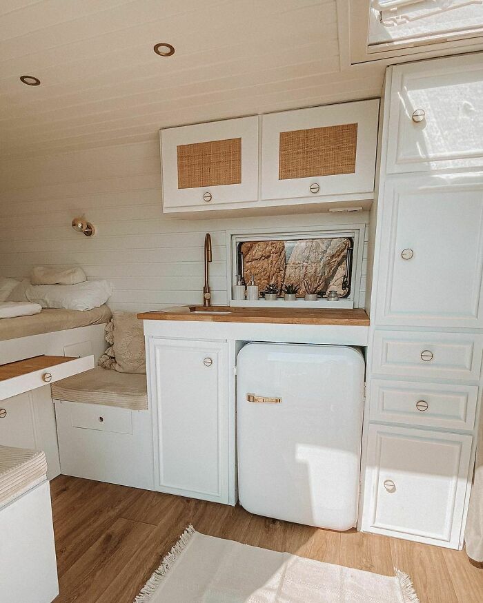 Compact tiny house kitchen with white fridge, wooden countertop, cabinets, and a small window with decor plants.