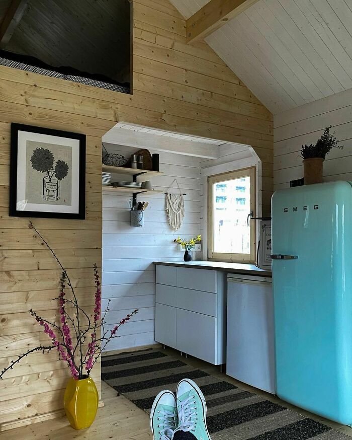 Cozy tiny house interior with wood panels and a retro Smeg fridge, featuring modern decor and a yellow vase beside the seating area.