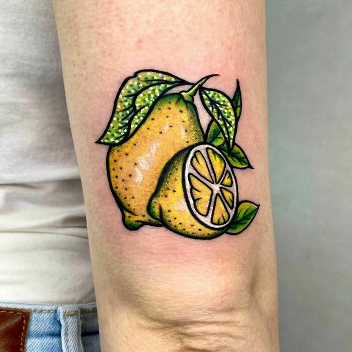 Lemon watercolor tattoo on arm, showcasing vibrant food-inspired ink art.