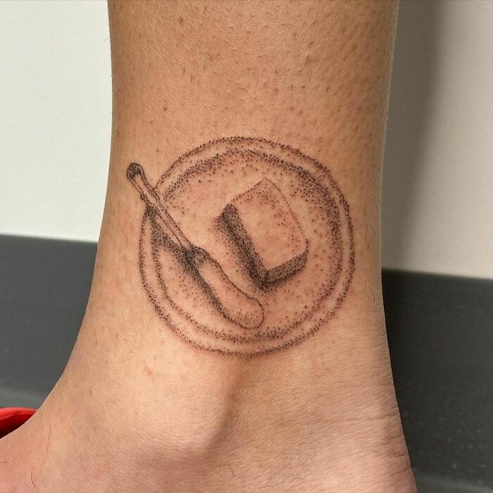 Food tattoo of a butter knife and butter on a plate, inked on skin.