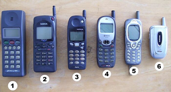 Six old mobile phones from different brands displayed on a wooden surface as classic old gadgets.