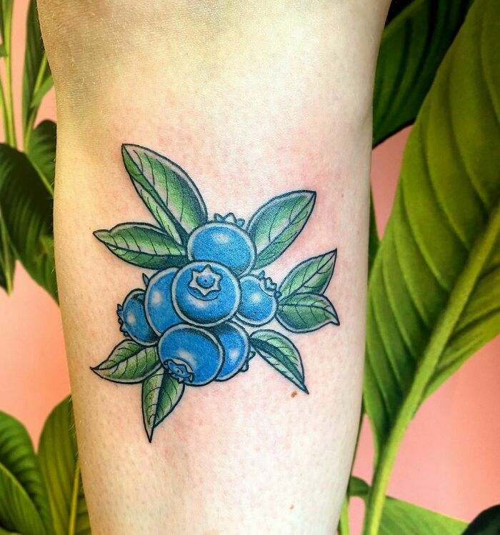 Blueberry tattoo on arm with vibrant leaves, showcasing delicious food-inspired ink.