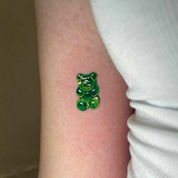 Green gummy bear tattoo on an arm, showcasing a unique food tattoo design.