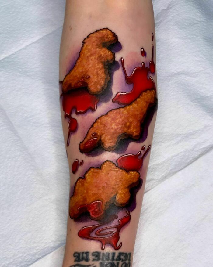 Food tattoo of chicken nuggets with red sauce, designed on a forearm.