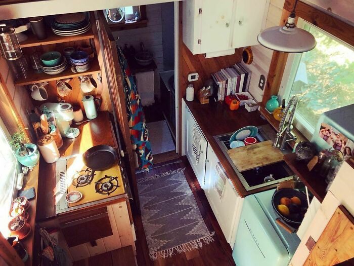 Cozy tiny house kitchen with white cabinets and brown countertop, featuring stove, sink, and rustic wooden accents.