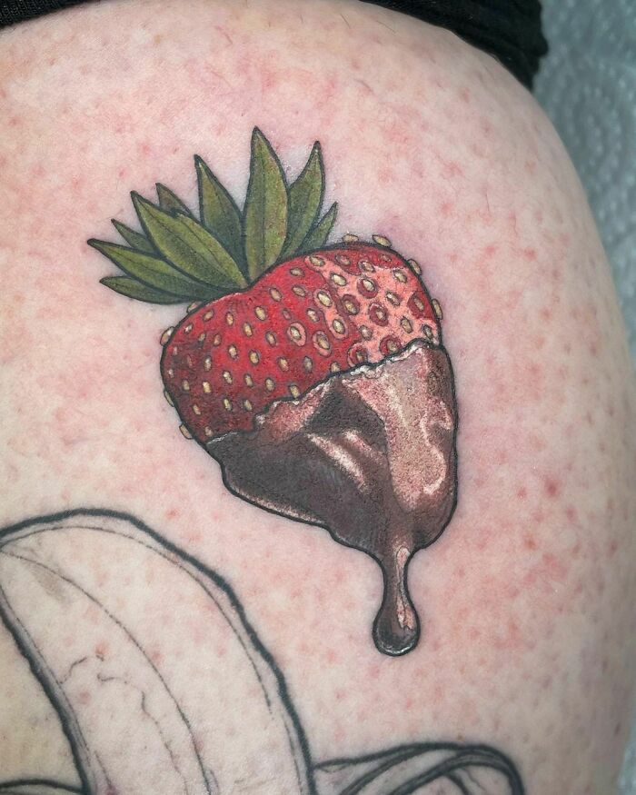 Delicious food tattoo of a chocolate-dipped strawberry on skin.