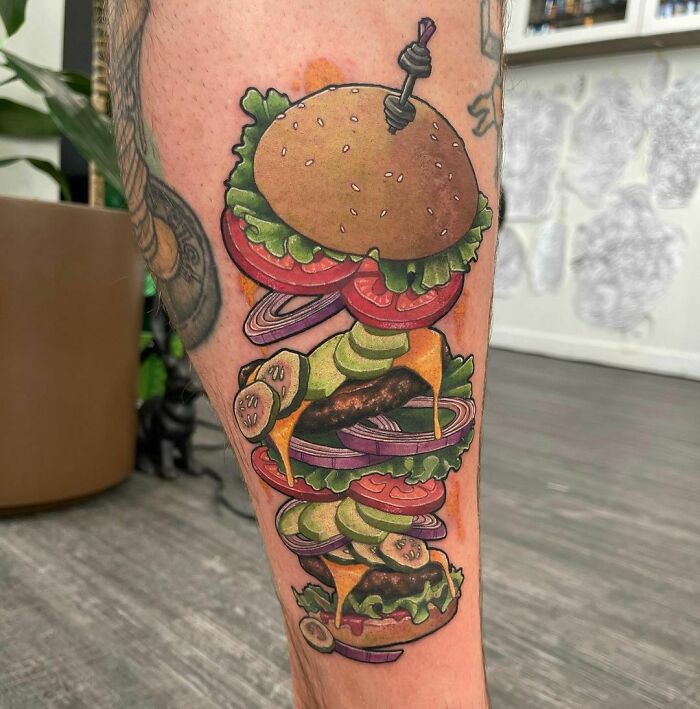 Burger watercolor tattoo showcasing vibrant layers on leg, combining art and food inspiration in a unique design.