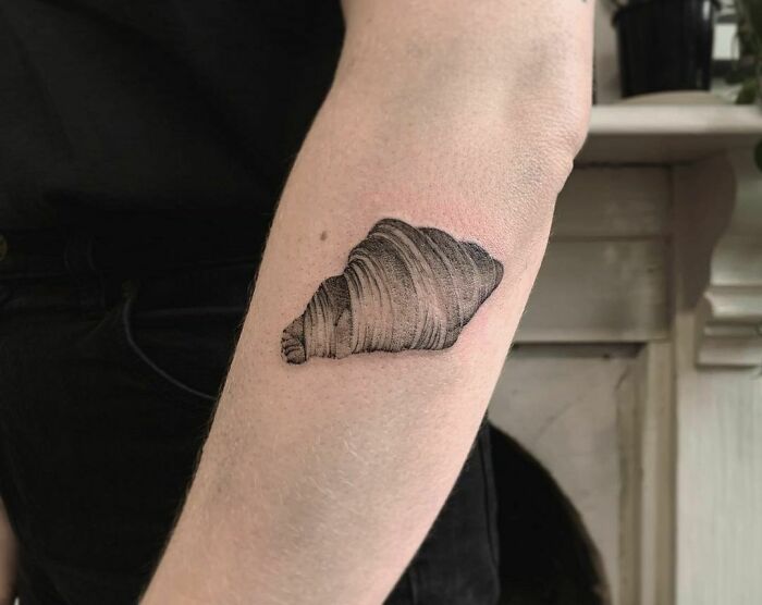 Minimalistic croissant tattoo on forearm, showcasing food-inspired body art.