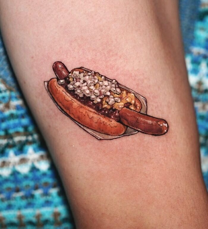 Food tattoo of a hot dog with toppings on a person's skin.