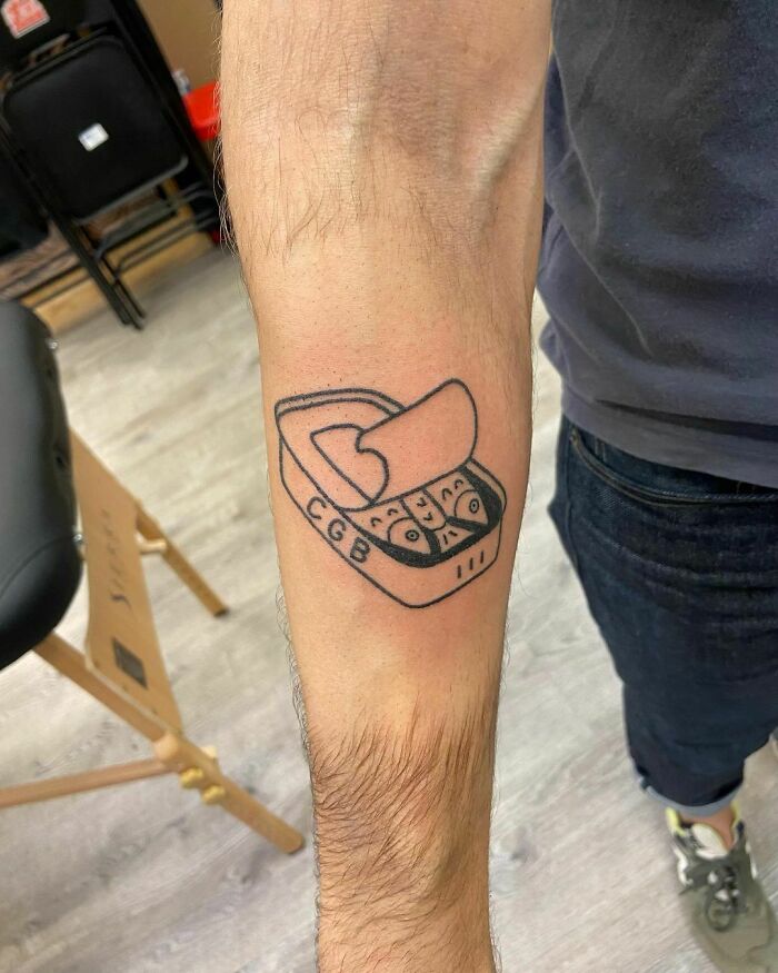 Tattoo of an open sardine can on an arm, showcasing unique food art.