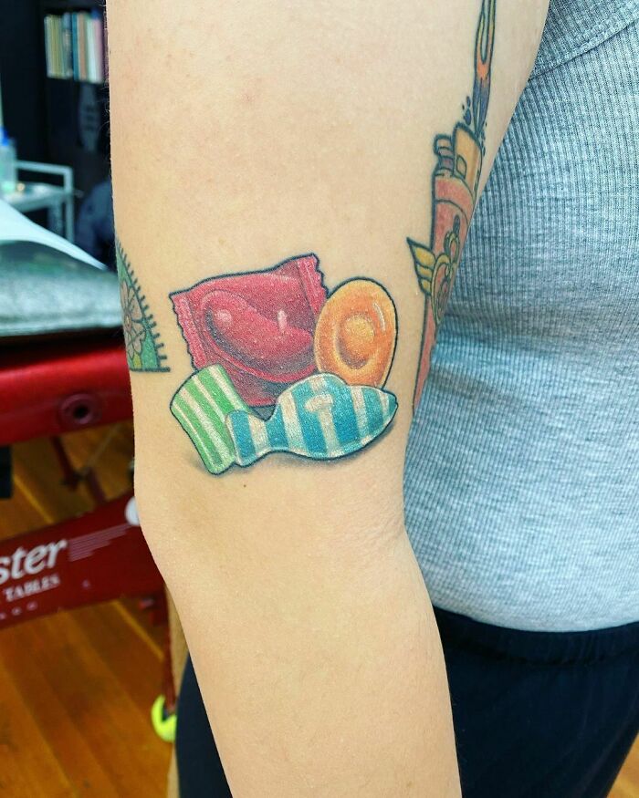 Watercolor candy tattoo featuring vibrant sweets on forearm, inspired by food art.