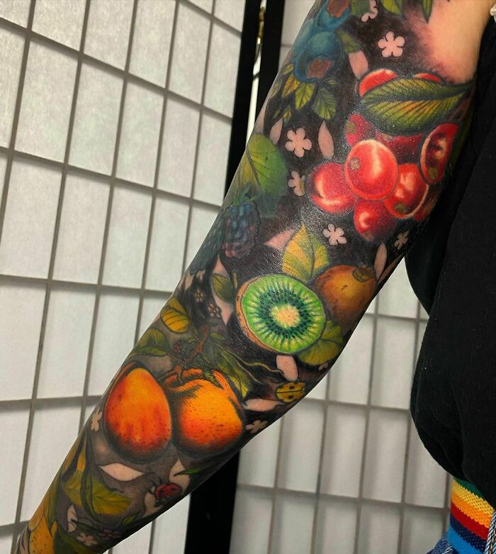 Watercolor fruit sleeve tattoo with vibrant oranges, kiwis, and berries, showcasing creative food tattoo ideas.