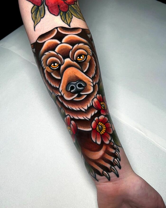 American traditional tattoo of a bear with red flowers on a forearm.