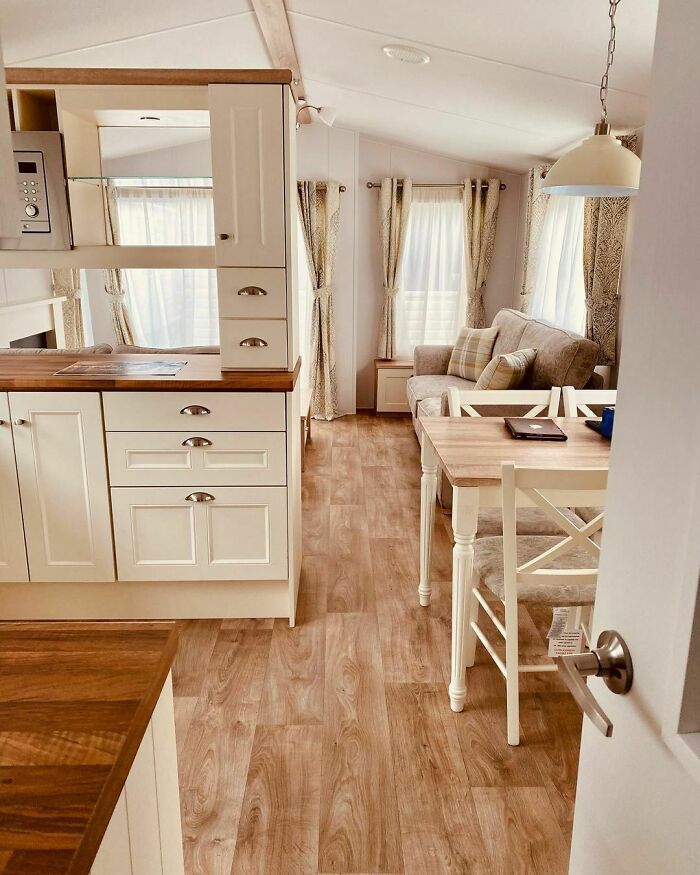 Modern tiny house interior with white cabinets, cozy seating, and wood flooring.