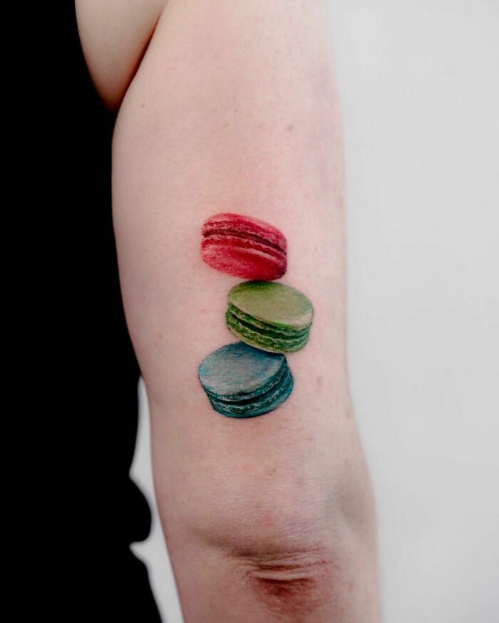 Colorful macaron food tattoo on arm, showcasing vibrant red, green, and blue designs.
