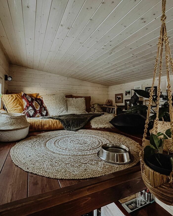 Cozy loft in a tiny house with wood paneling, plush cushions, and potted plants, showcasing irresistible tiny house designs.