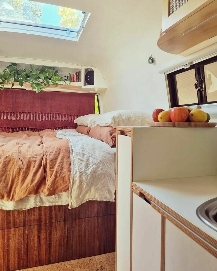 Cozy bed with white and salmon sheets inside a tiny house featuring natural light and compact living space design.