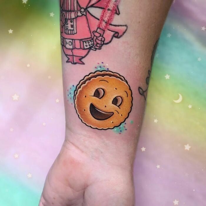 Smiling cookie food tattoo on wrist with colorful background.
