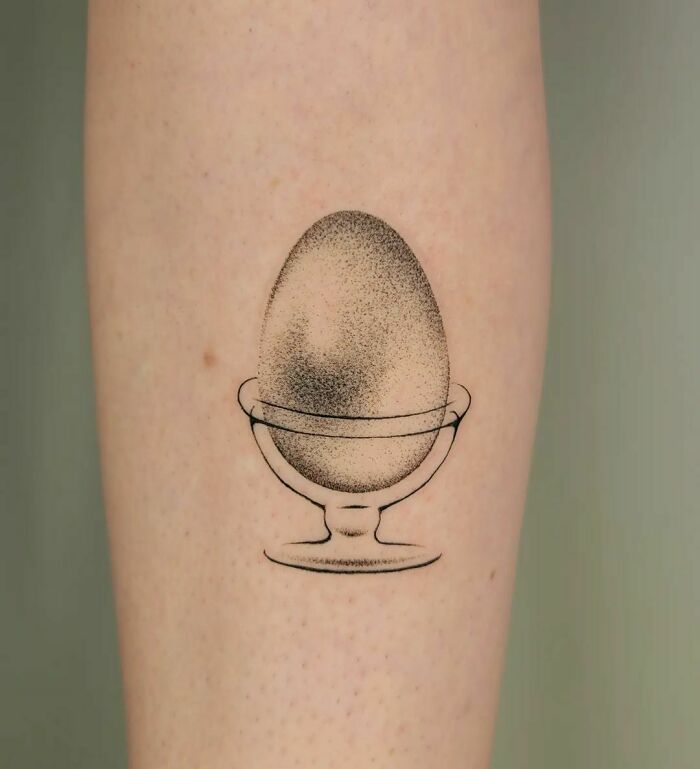 Food tattoo of an egg in a cup on an arm, showcasing delicate shading and minimalist design.