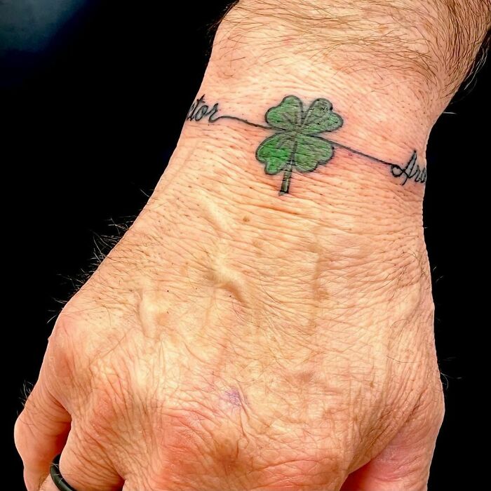 Wrist tattoo of a four-leaf clover with cursive text, showcasing a creative statement design.