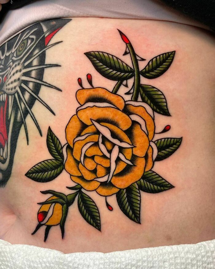 Yellow rose American traditional tattoo with bold outlines and green leaves.