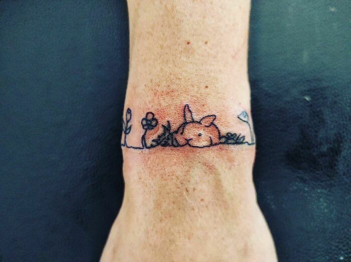 Minimalist wrist tattoo of a cute bunny with flowers and grass.