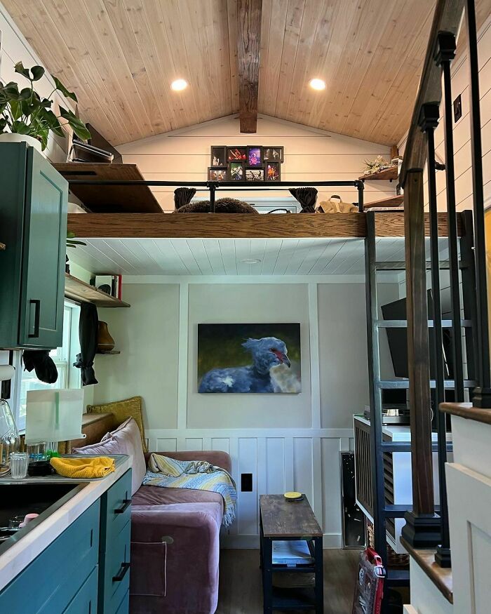 Cozy tiny house interior with loft, colorful kitchen, and animal painting on white wall.