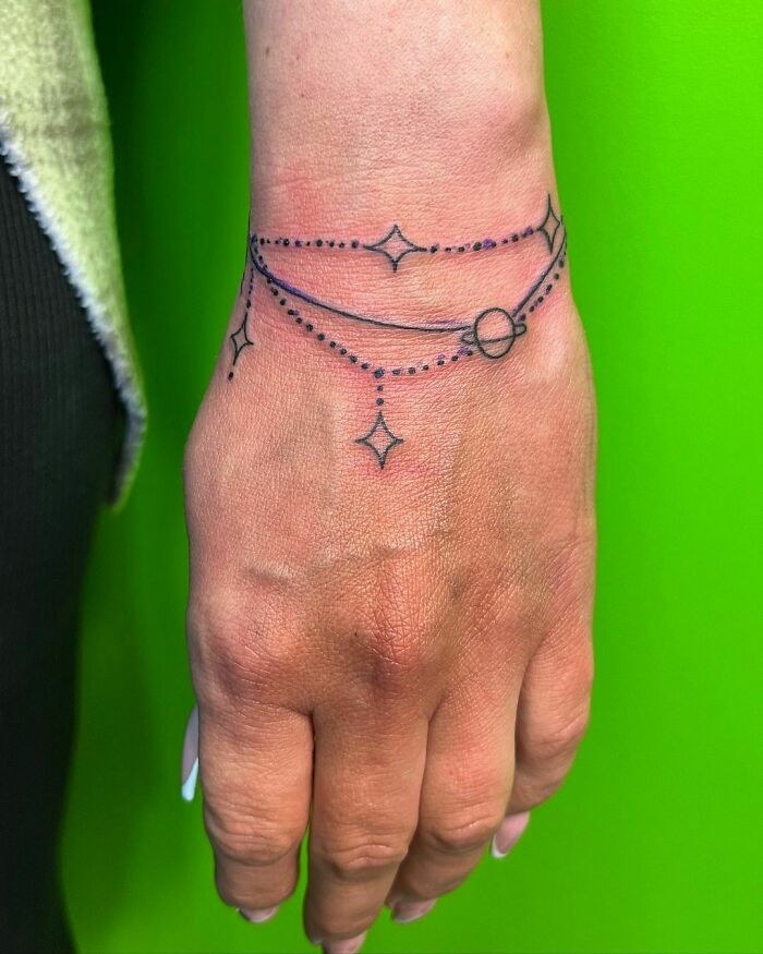 Minimalist wrist tattoo with stars and lines against a bright green background.
