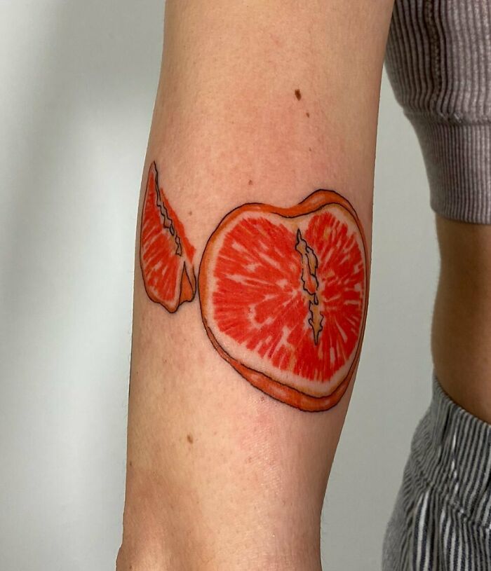 Watercolor tattoo of sliced orange citrus fruit on arm, a vibrant food tattoo idea.