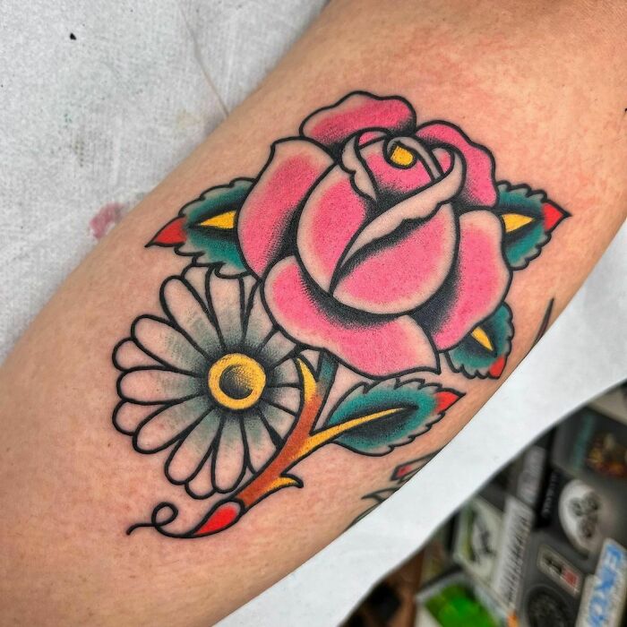 American traditional tattoo featuring a vibrant rose and daisy on an arm.