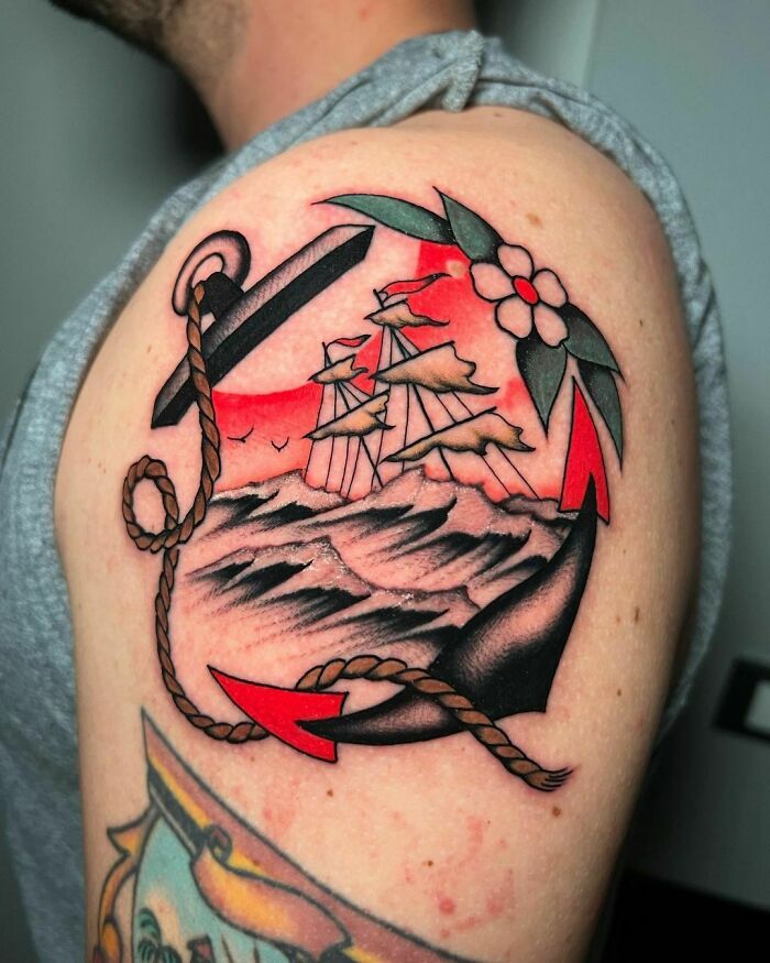 American traditional tattoo on arm featuring a ship, anchor, and flower in bold colors.