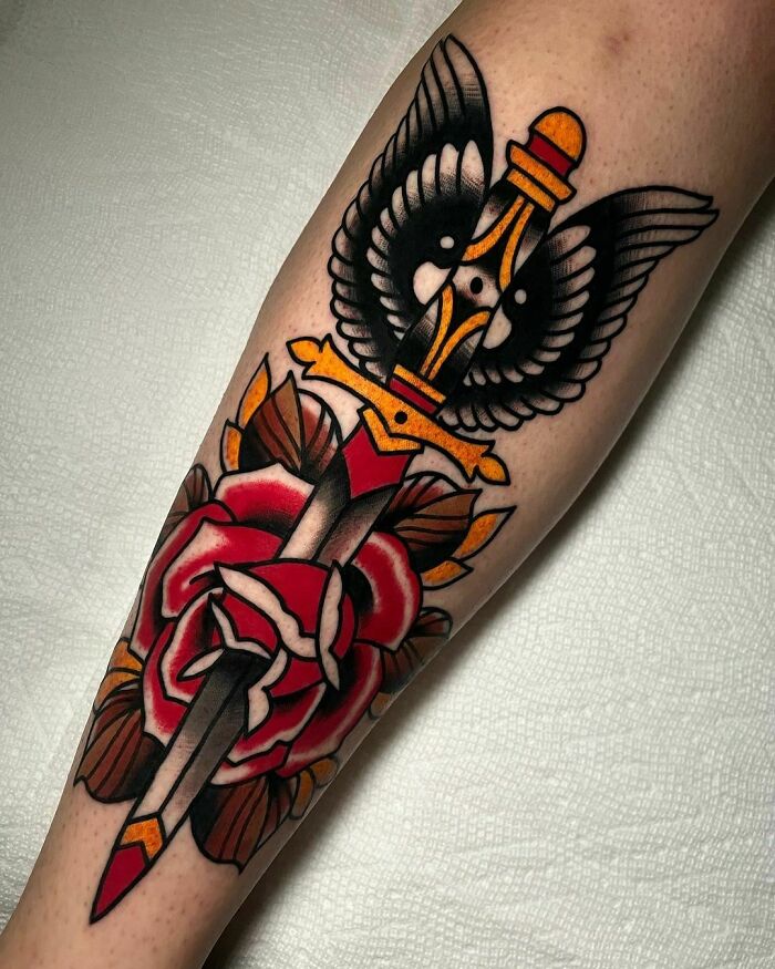 American traditional tattoo of a dagger and rose, featuring bold colors and classic design elements on an arm.