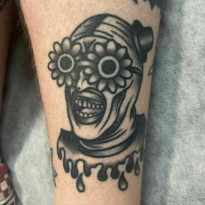 American traditional tattoo featuring a unique face with flowers for eyes on a forearm, showcasing bold black ink design.